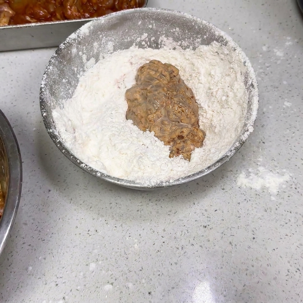 水に浸した後のチキンを、乾いた小麦粉のボウルの中で転がしている様子。