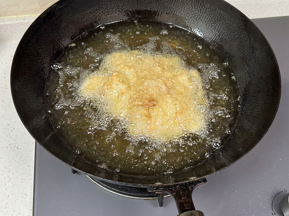 深い中華鍋の中で、油の中で泡立ちながら揚がっているチキンの様子。