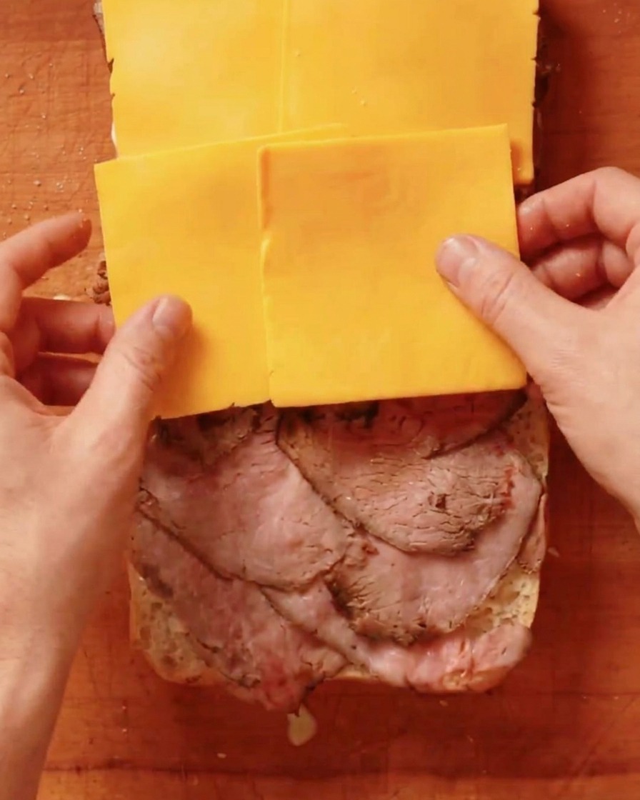 牛肉の上にチェダーチーズのスライスを並べている様子。