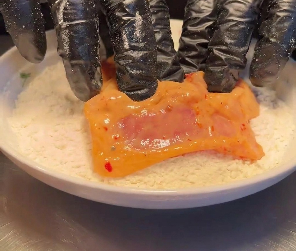 マリネした鶏もも肉を平らな皿に入った小麦粉に押し付けている様子。