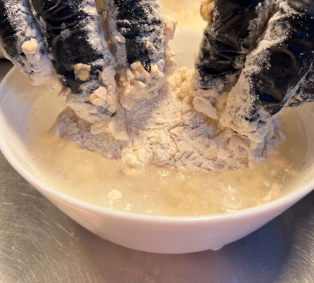 粉をまぶしたチキンを、水を入れたボウルに短時間浸している様子。