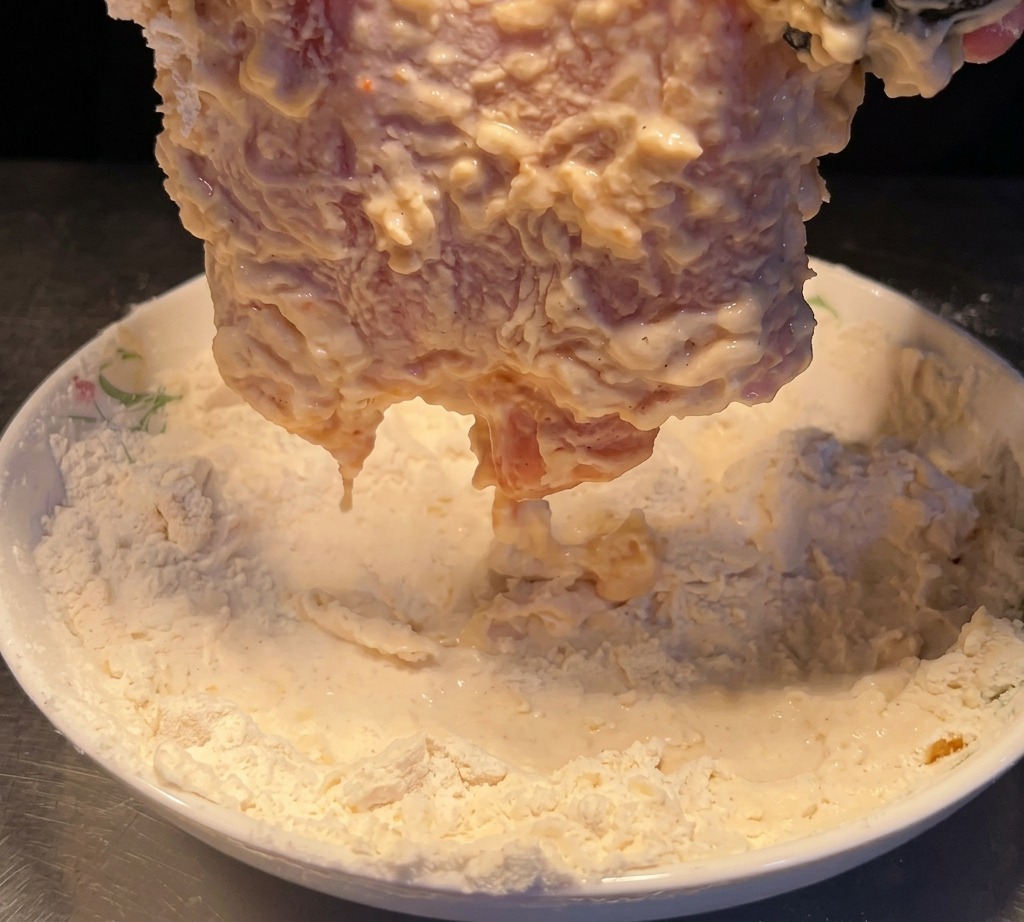 水にくぐらせたチキンを、再度小麦粉の皿で粉をまぶしている様子。