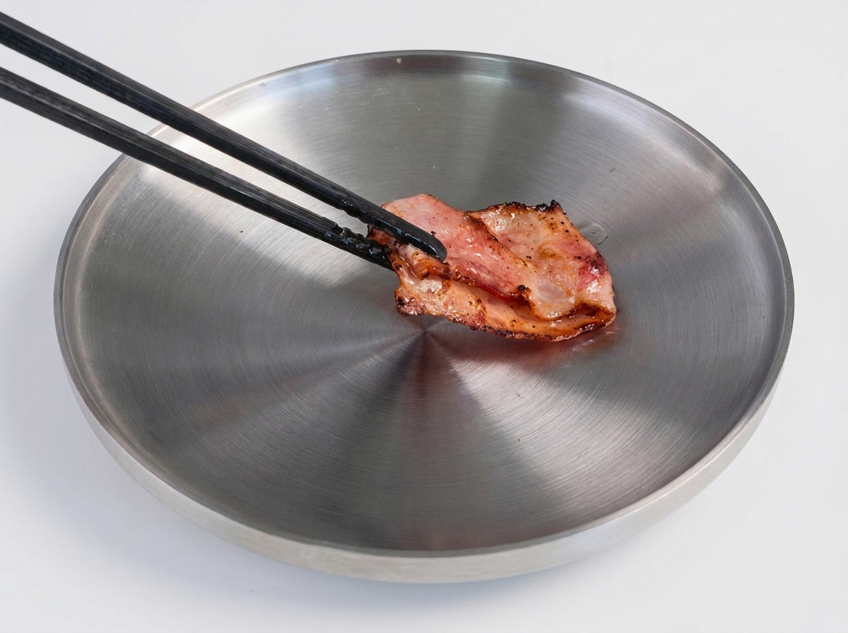 熱したフライパンの中で、こんがりと焼き目のついたビーフパティをフライ返しで裏返している様子。