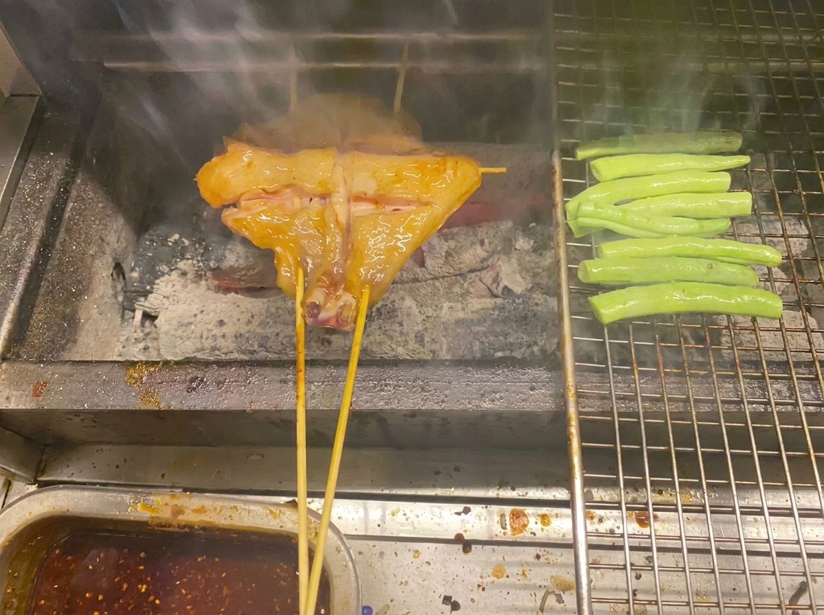 炭火のグリルで焼かれる鶏肉といんげん。