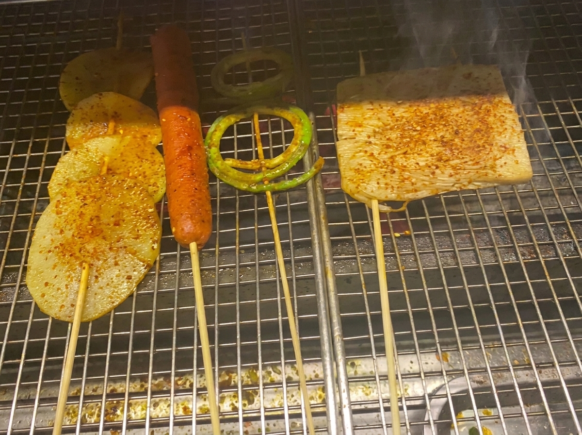 バーベキューソースを塗られ、チリパウダーが振られた焼き野菜とソーセージ。