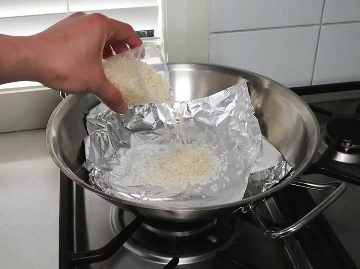アルミホイルを敷いた中華鍋に米とウッドチップを広げている様子。