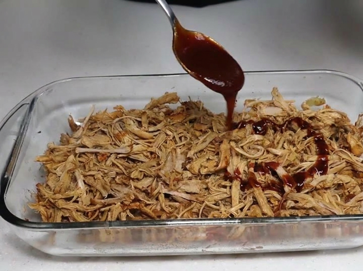 ほぐした豚肉にBBQソースをかけている様子。