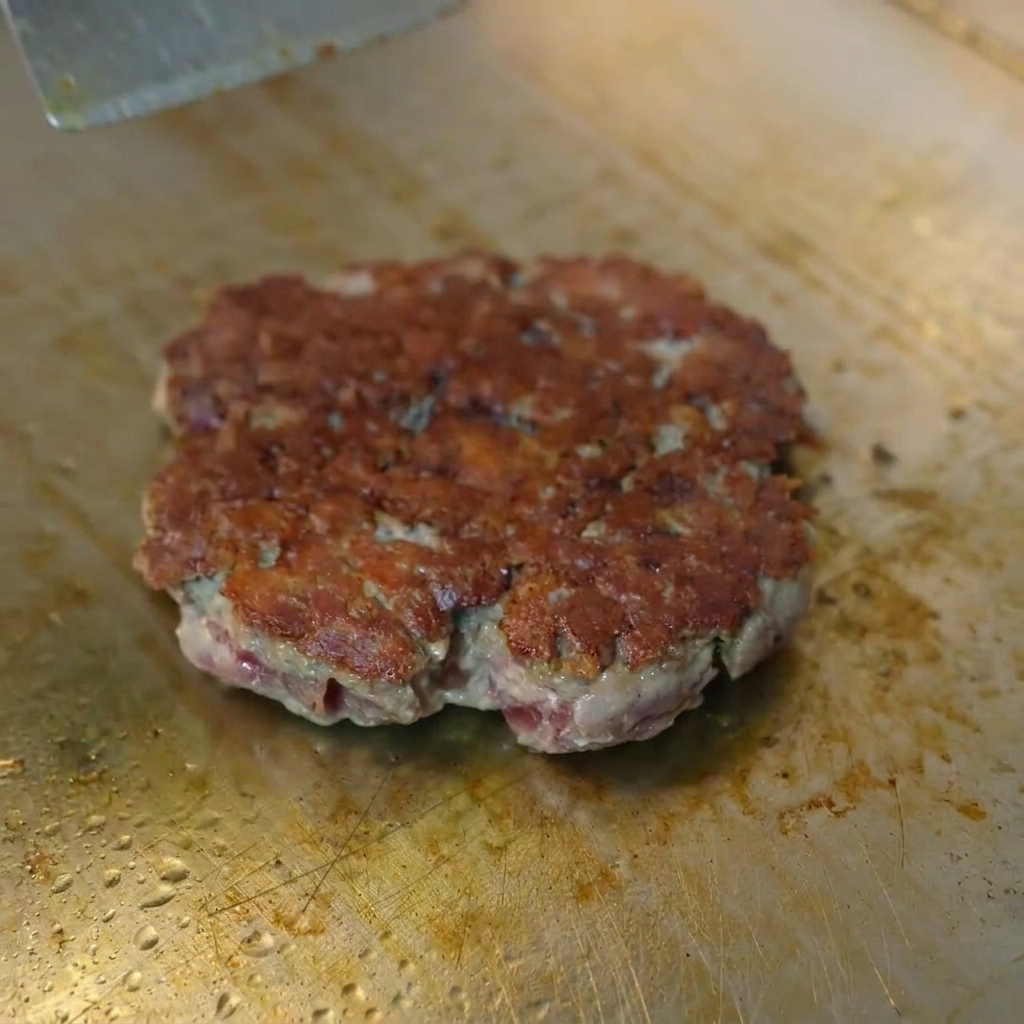 金属製のドームを被せ、焼き色のついたパティの上でチーズが溶けている様子。