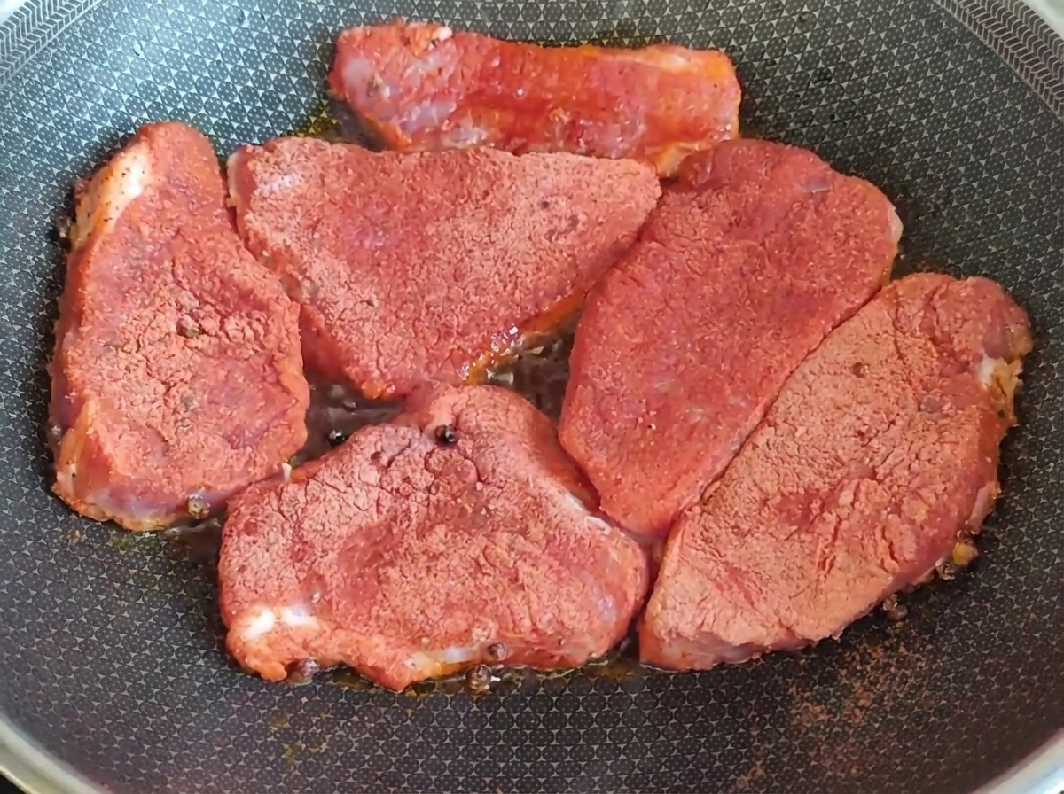 シーズニングをまぶした厚切りの豚肉をフライパンで焼いている様子。
