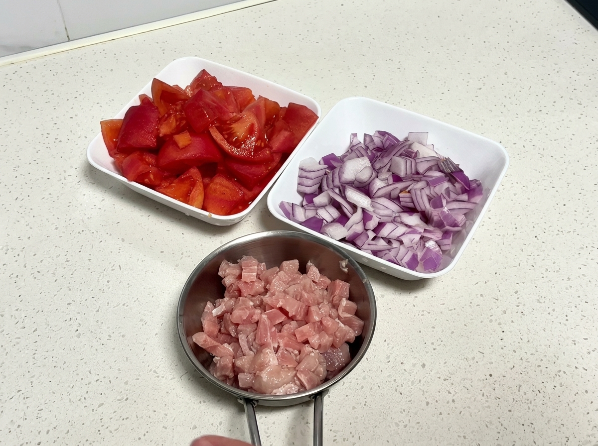まな板の上にカットされたトマト、みじん切りの赤玉ねぎ、豚ひき肉が並んでいる様子。