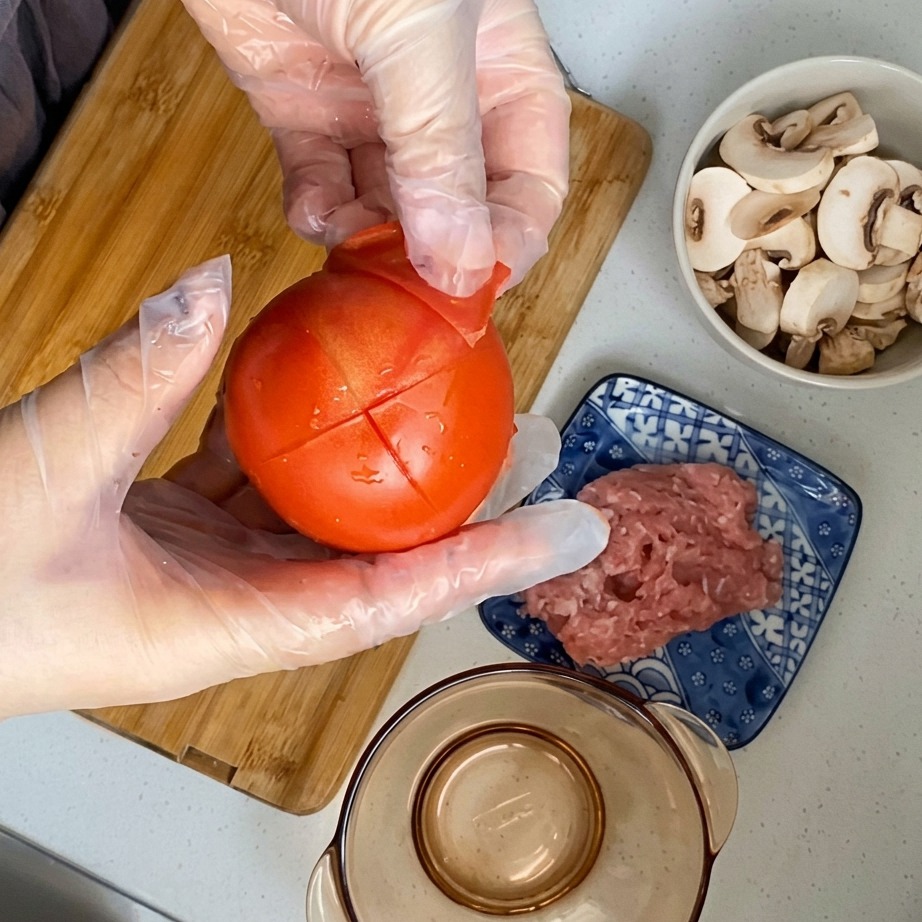 湯むきしたトマトの皮を、十字の切り込みから剥がしている様子。