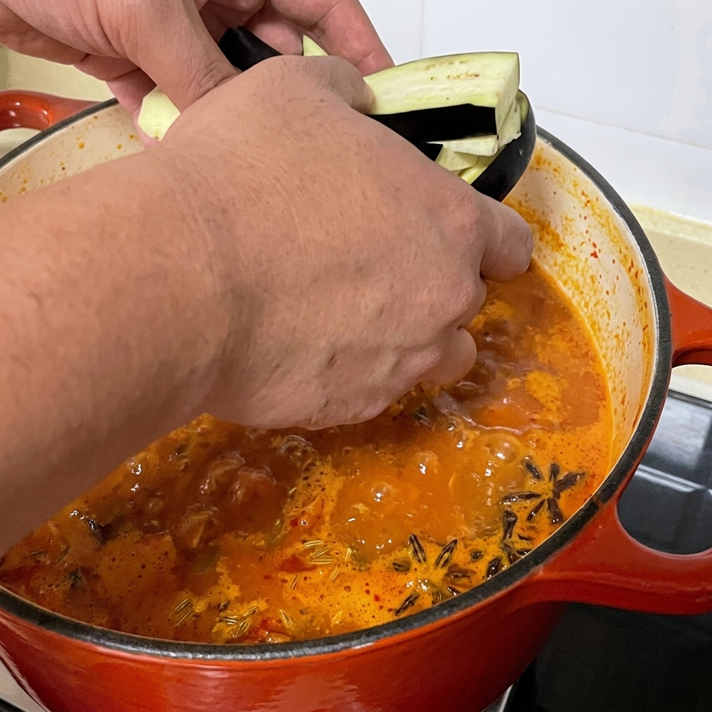 細切りにしたナスを、スパイシーなあさりスープの鍋に加えている様子。