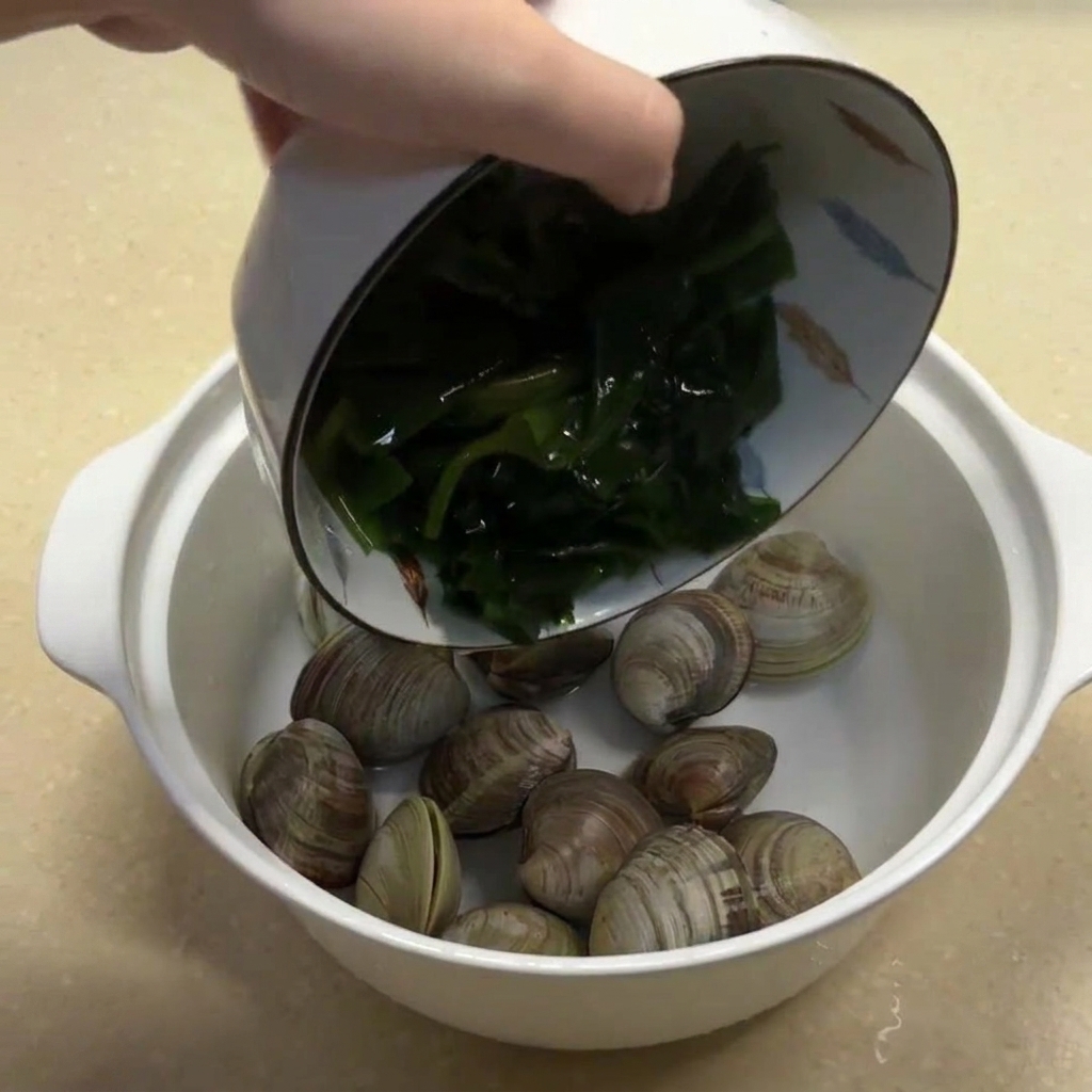 あさりの入ったボウルに、水で戻したわかめと千切り生姜を加えている様子。