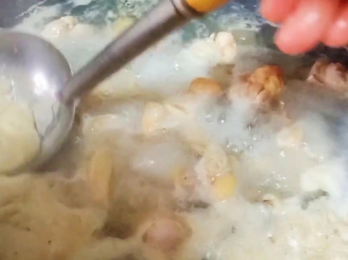 沸騰したお湯に浮かぶ鶏肉のアクを、おたまですくい取っている様子。