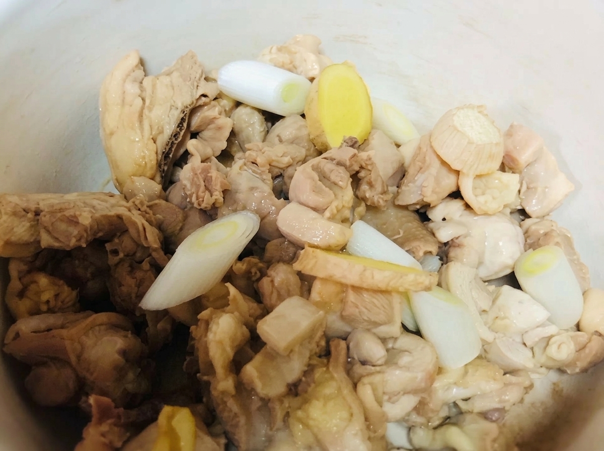 土鍋に入った鶏肉に、ネギ、生姜、調味料を加えている様子。