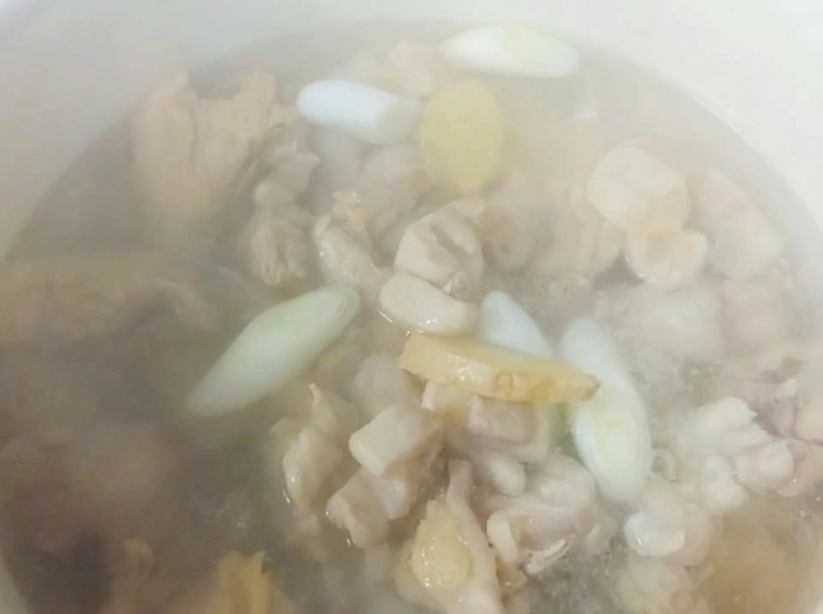 鶏肉と香味野菜が入った鍋に、湯気の立つ熱湯を注いでいる様子。