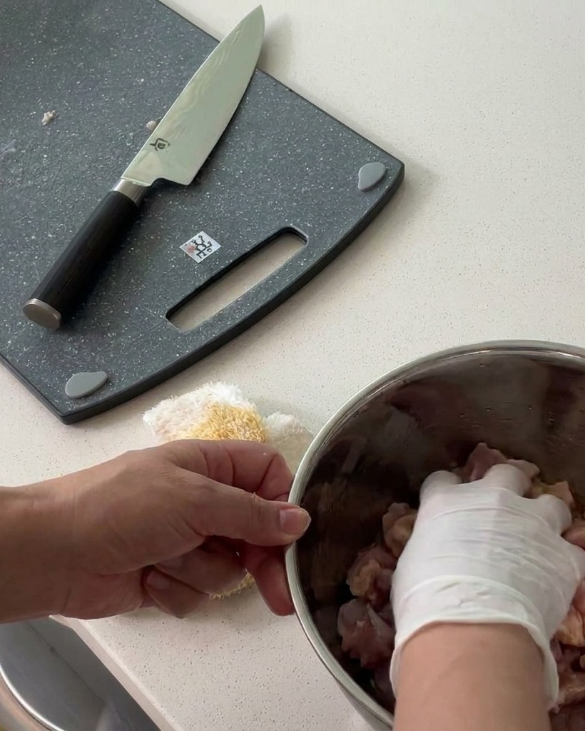 金属製のボウルで、カットした鶏肉に調味料を揉み込んでいる様子。