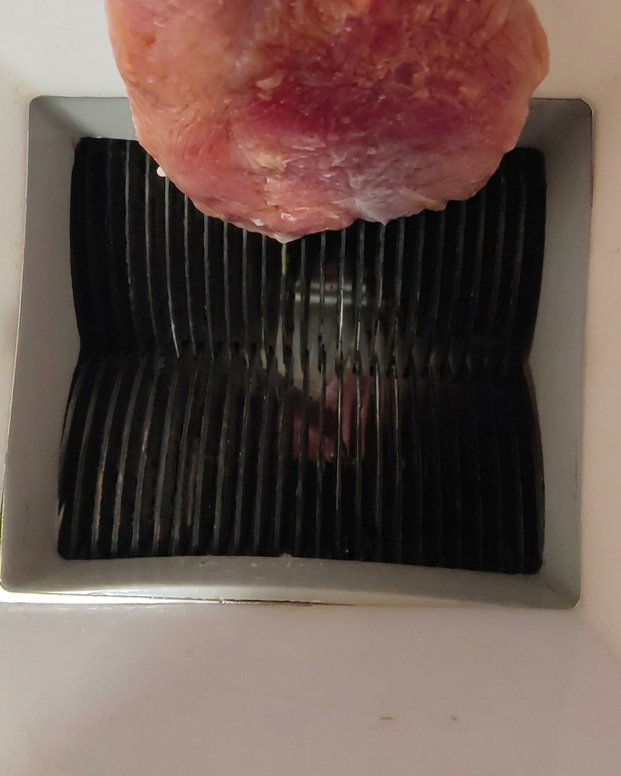 生の鴨肉をミートスライサーの上部から入れている様子。