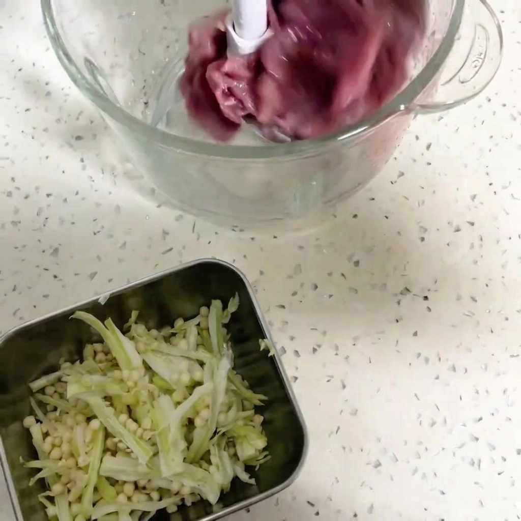 真っ赤な鴨肉の塊とオクラの種が入った、ペースト状にする準備ができているフードプロセッサーのボウル。