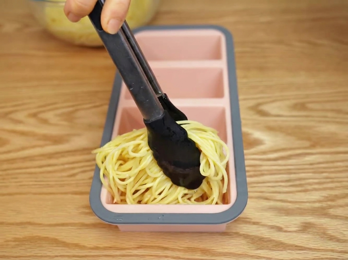 茹で上がったパスタをトングでシリコン型に入れている様子。