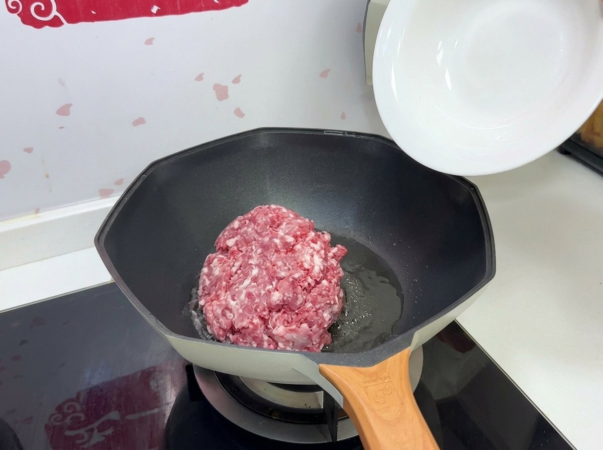 熱したフライパンにひき肉を入れる様子。