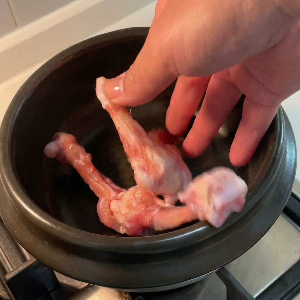 黒い陶器の鍋に鶏の骨を入れる様子。