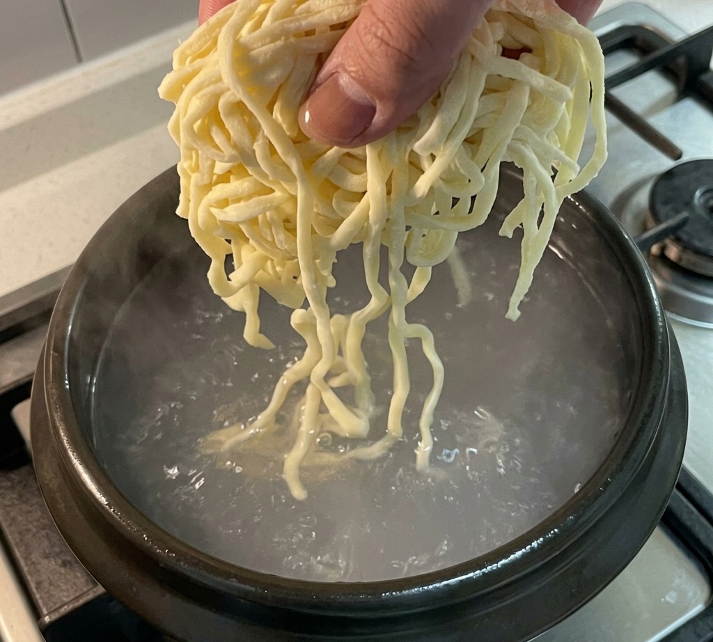 煮立っているスープの中に麺を入れる様子。