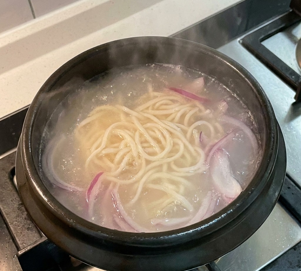 スライスした赤玉ねぎを麺と一緒に煮込んでいる様子。