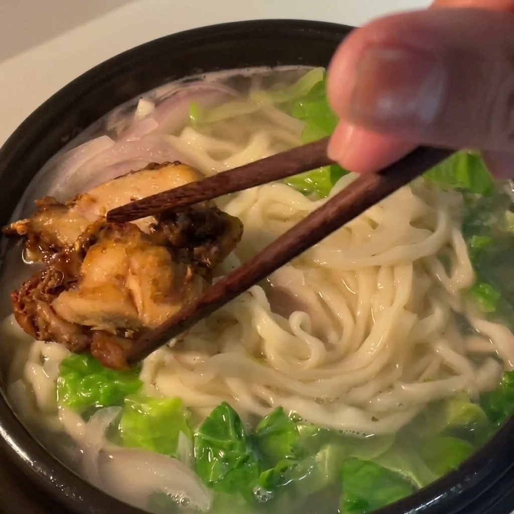 麺の上にローストチキンを盛り付けている様子。