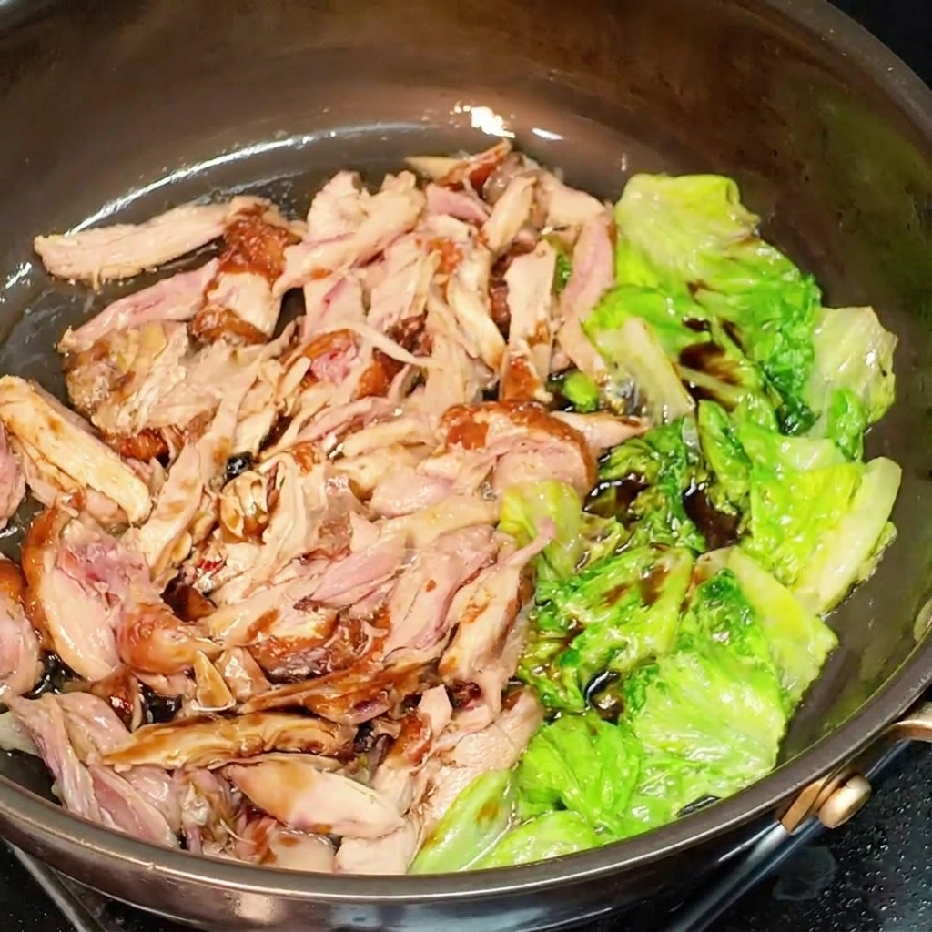 フライパンの中で、細切り鶏肉とレタスに醤油が馴染むよう混ぜ合わせている様子。