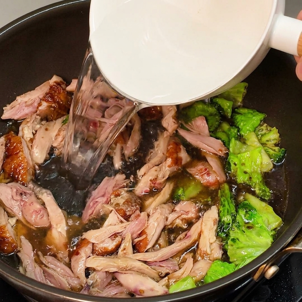 熱湯をフライパンに注ぎ、鶏肉とレタスと混ぜ合わせてスープを作っている様子。