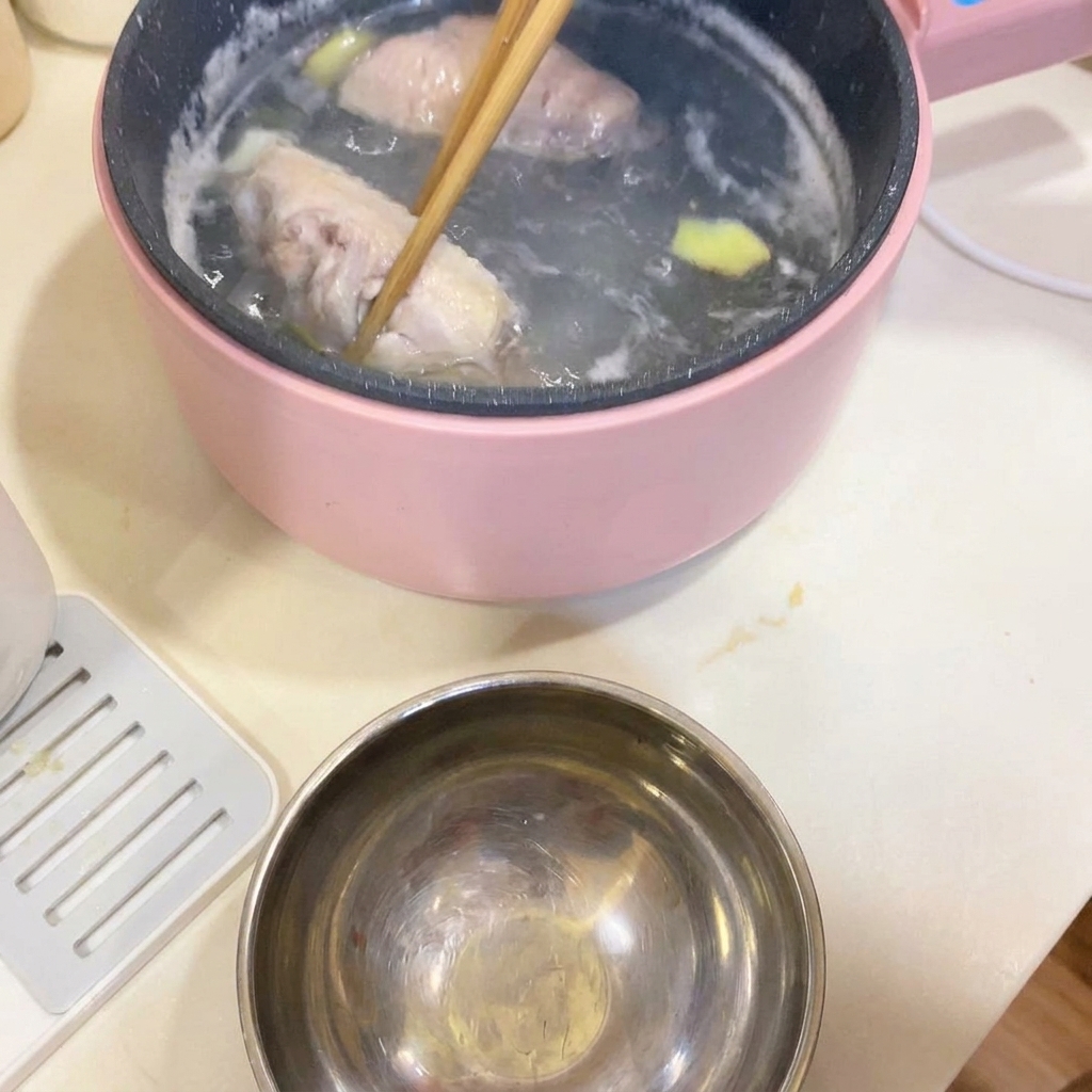 鍋から菜箸で下茹でされた鶏手羽先を取り出している様子。