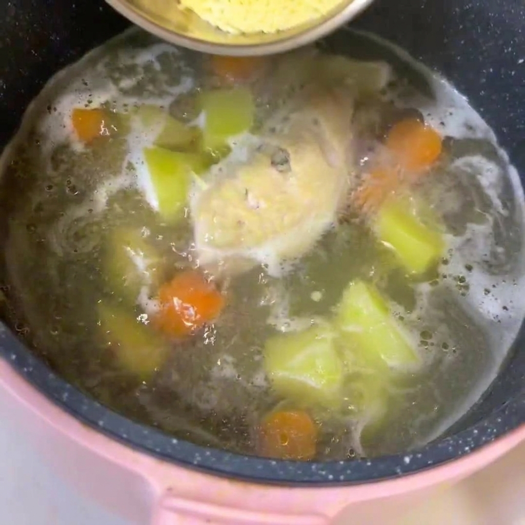 鶏肉、じゃがいも、にんじんが煮込まれているスープの鍋に、ベビーヌードルを加えてかき混ぜている様子。