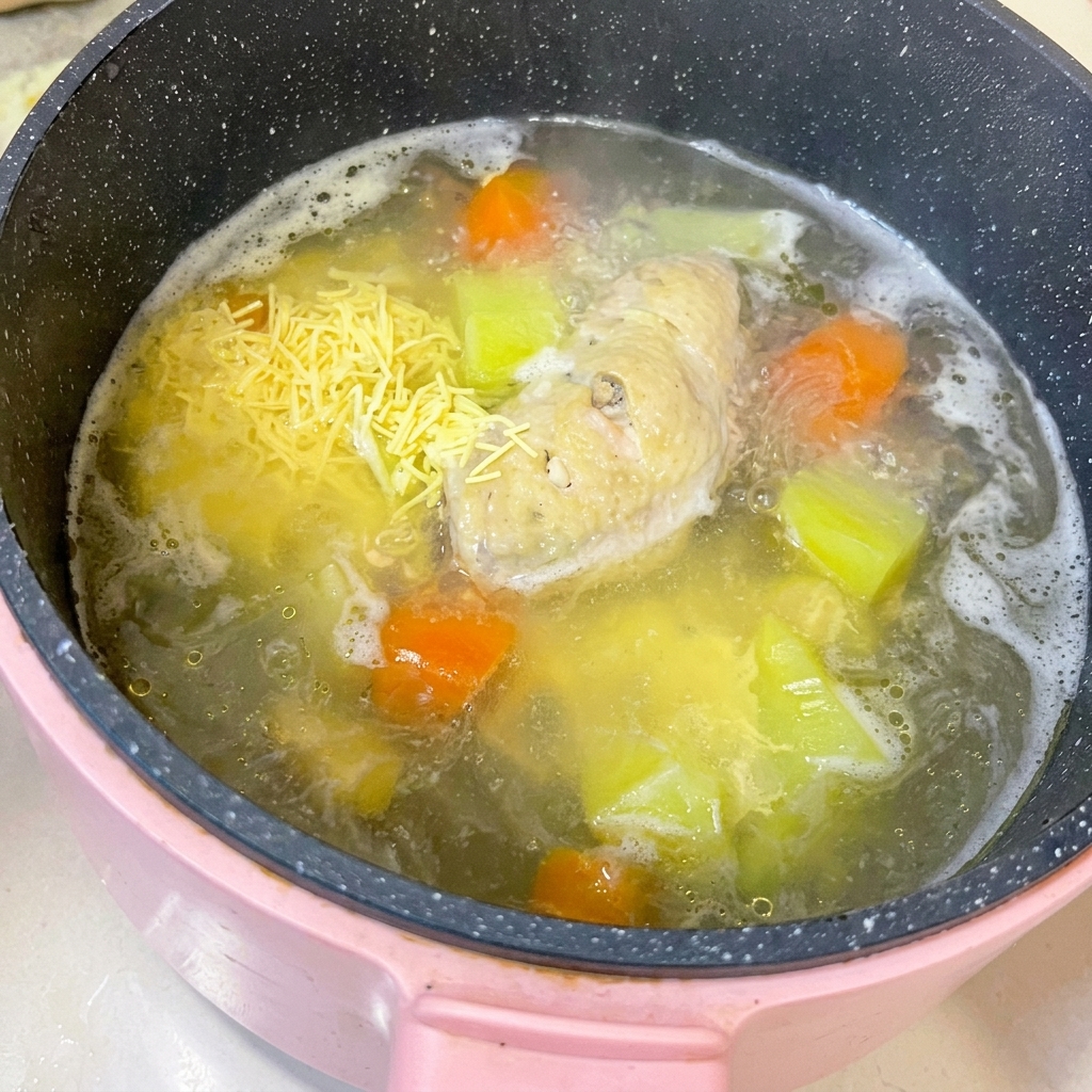 まな板に置かれた茹でた鶏手羽先を、包丁を使って骨から肉を外している様子。