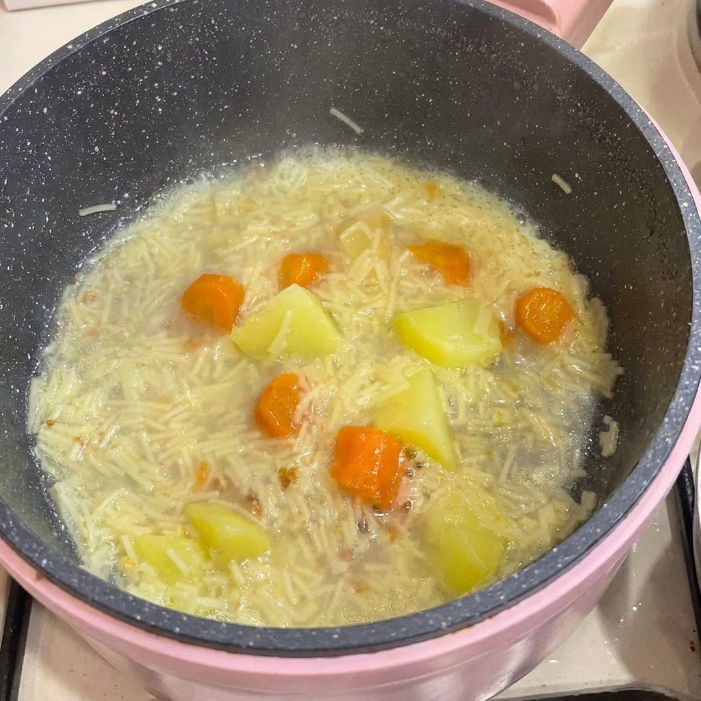骨から外した鶏肉を、ベビーヌードルや野菜が煮込まれた鍋に戻している様子。