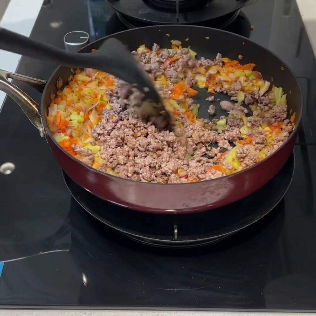 炒めた肉と野菜をフライパンの中で混ぜ合わせている様子。
