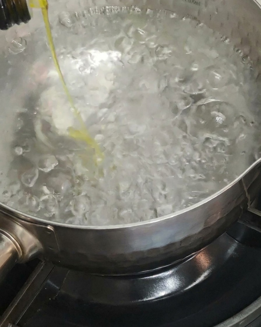沸騰したたっぷりのお湯が入った鍋にオリーブオイルを垂らしている様子。
