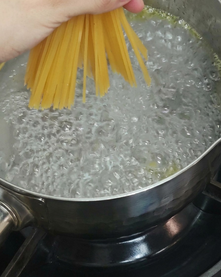 乾燥スパゲッティの束を手に持ち、ぐつぐつと沸騰した鍋に沈めている様子。