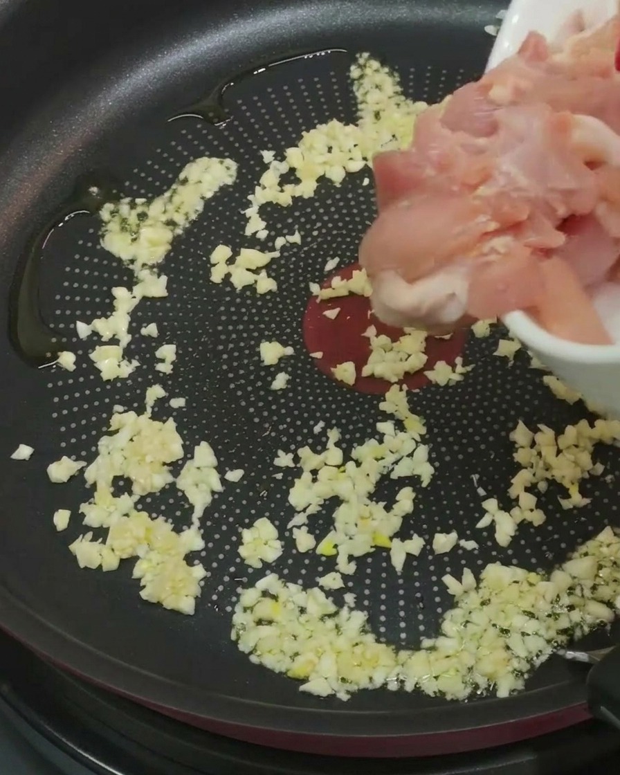 にんにくとオイルが入ったフライパンに、下味をつけた鶏肉を加えている様子。