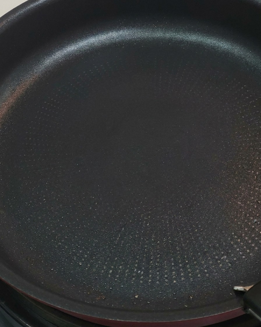 赤いトングを使ってフライパンの鶏肉を裏返し、表面がきつね色に焼けている様子。