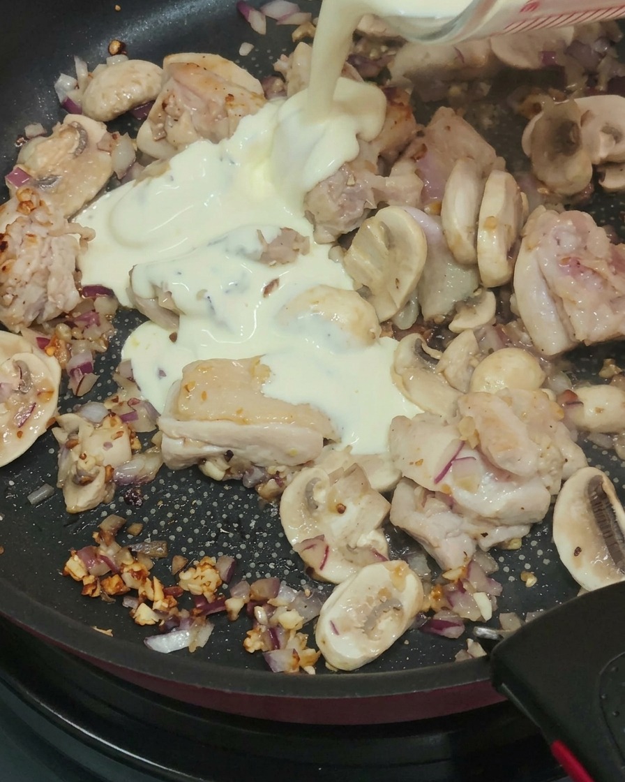 炒めた鶏肉、マッシュルーム、玉ねぎが入ったフライパンに、生クリーム、牛乳、白ワインを注いでいる様子。