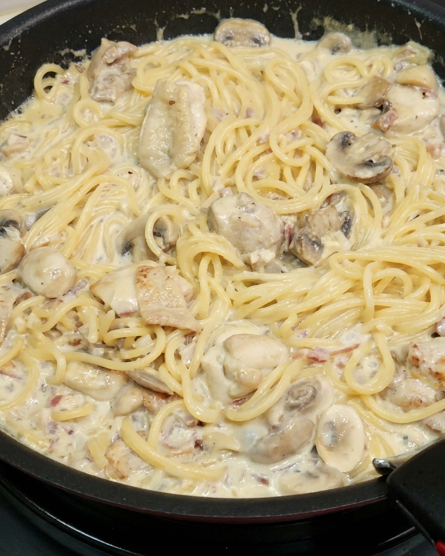 鶏肉やマッシュルームが入った濃厚なクリームソースとパスタをフライパンで絡めている様子。