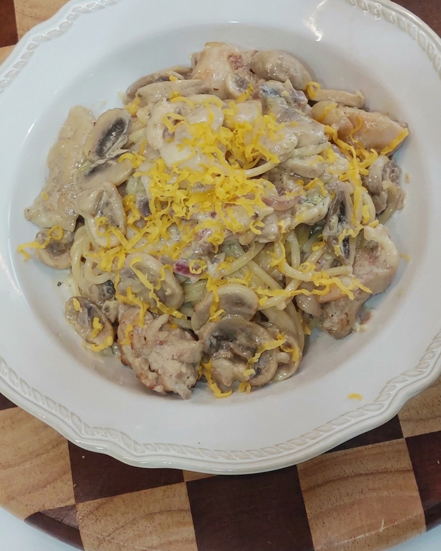 盛り付けられたクリームパスタの上に、黄色のチーズの塊を削りかけている様子。