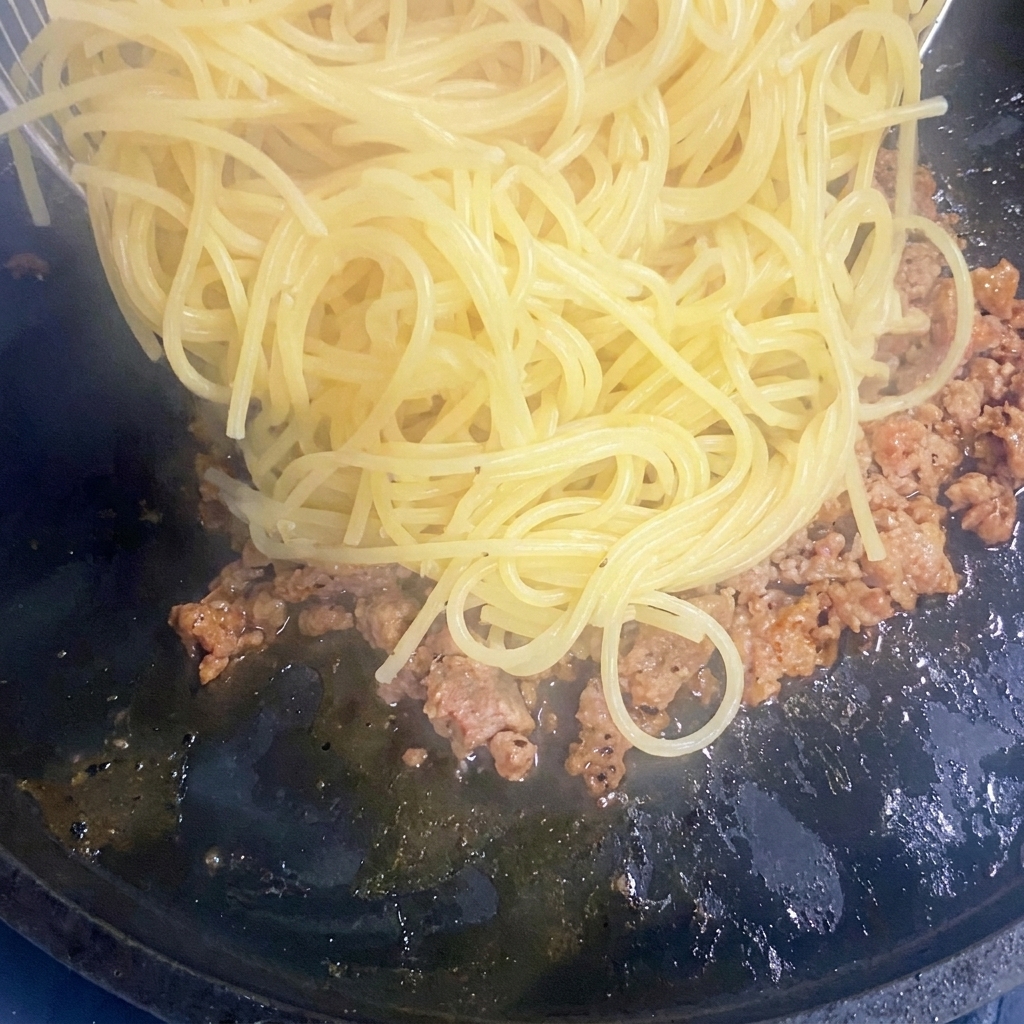 炒めたひき肉の入ったフライパンに茹でたスパゲッティを加える様子