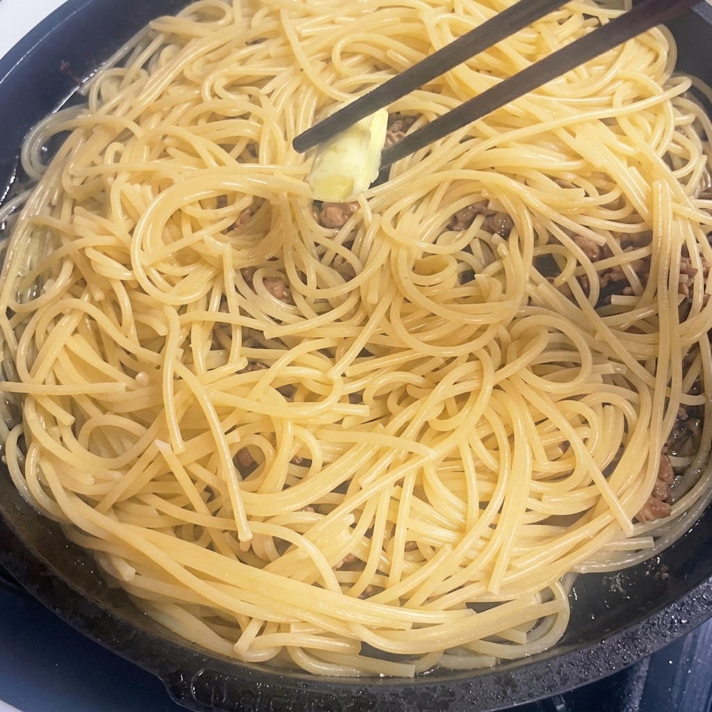 熱いパスタとひき肉の入ったフライパンで溶けるバター