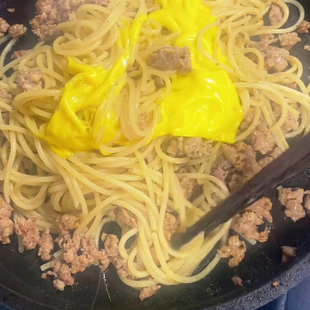 スキレットの中でスパゲッティとミートソースに溶けたチーズを絡ませている様子