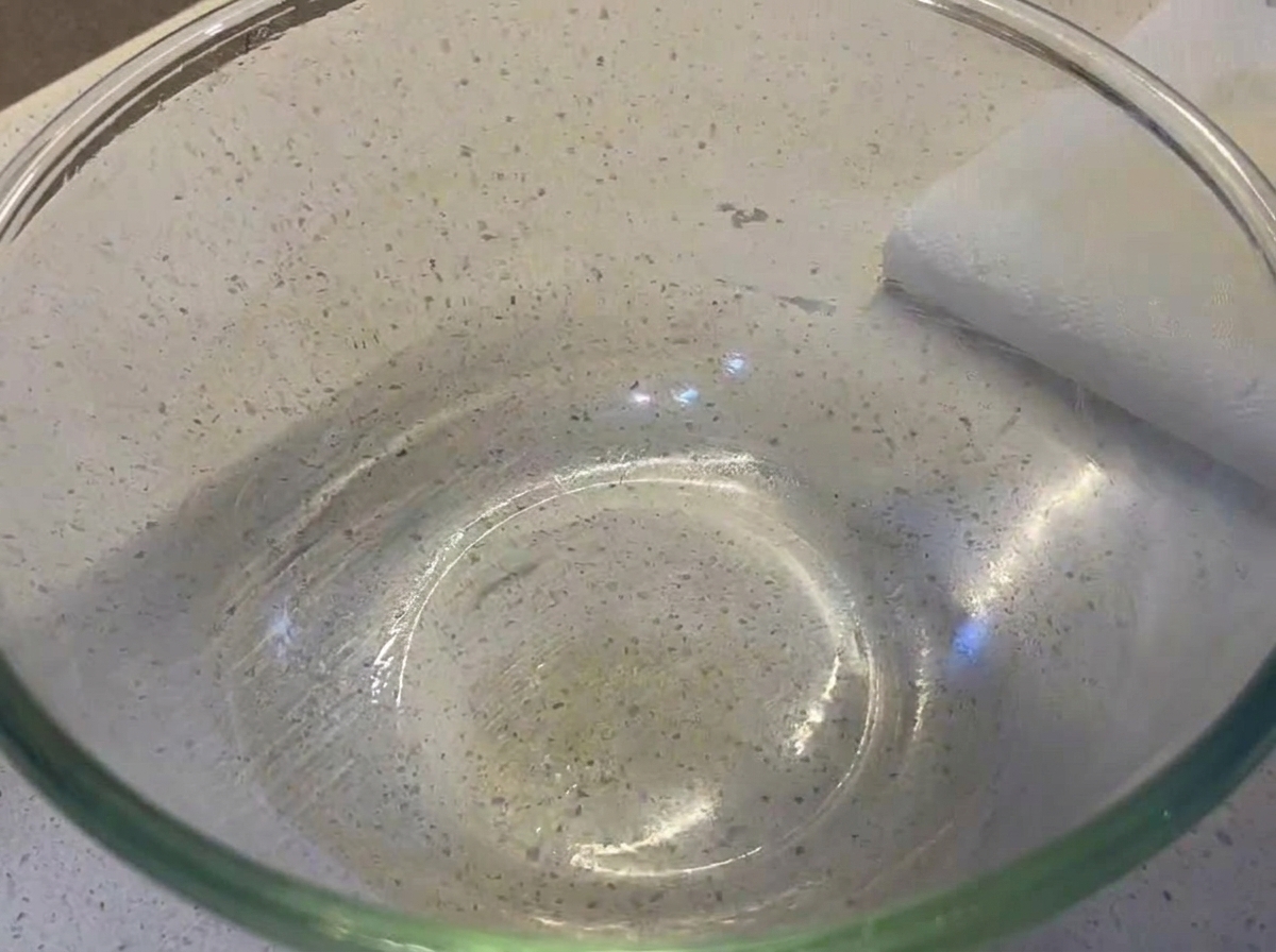 薄く油を塗った透明なガラスボウルの中に、丸く滑らかなピザ生地が置かれている様子。