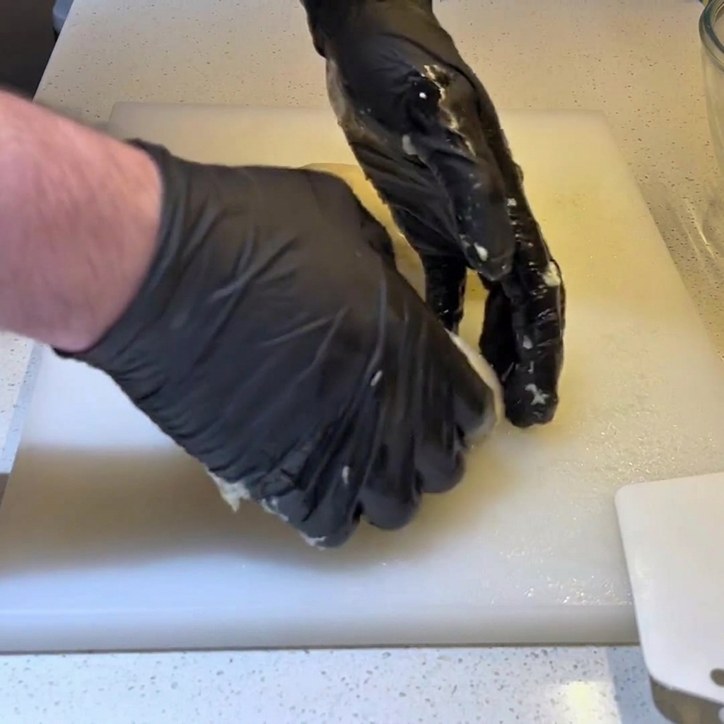 手袋をした手で生地の端を内側に巻き込み、表面が張った丸い玉を作っている様子。