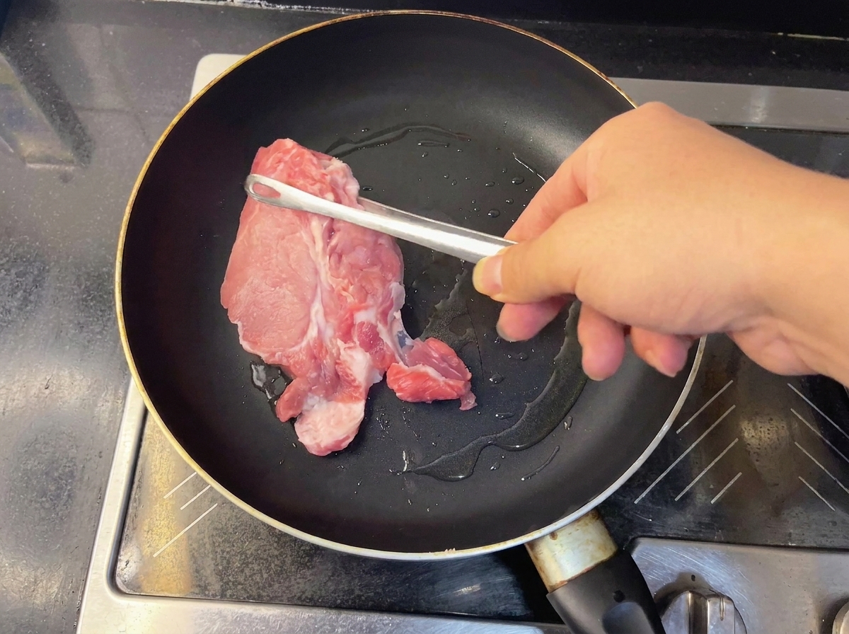 熱したフライパンで焼かれる豚肩ロース肉。