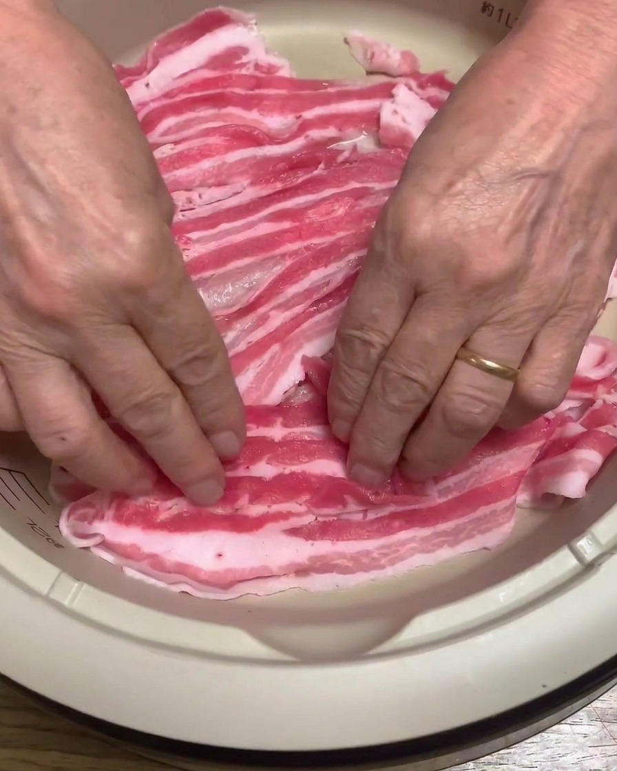 電気鍋の底に豚バラ肉をきれいに並べている様子。